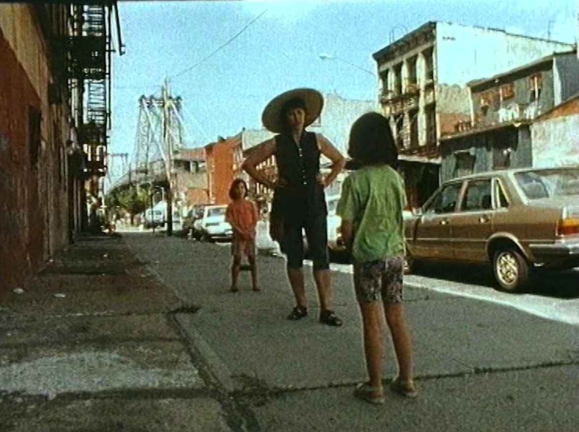 Archival footage of Emilija and Ona as young girls with their mother, in a wide sun hat, on a Williamsburg street